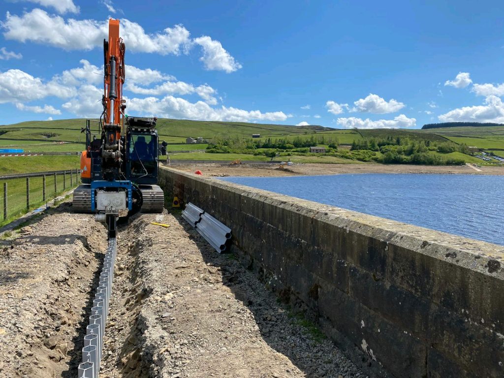 Photo of an excavator mounted vibrator installing plastic sheet piling